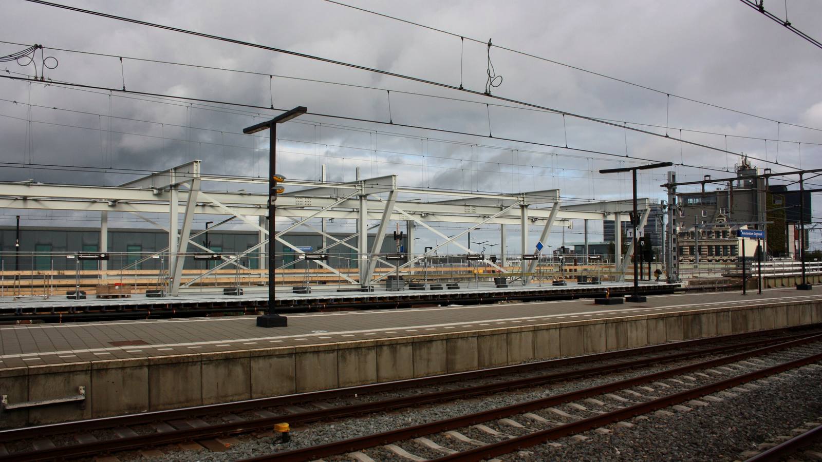 Perron van station Amsterdam Centraal met een stalen constructie en bouwhekken tijdens werkzaamheden, onder een grijze lucht