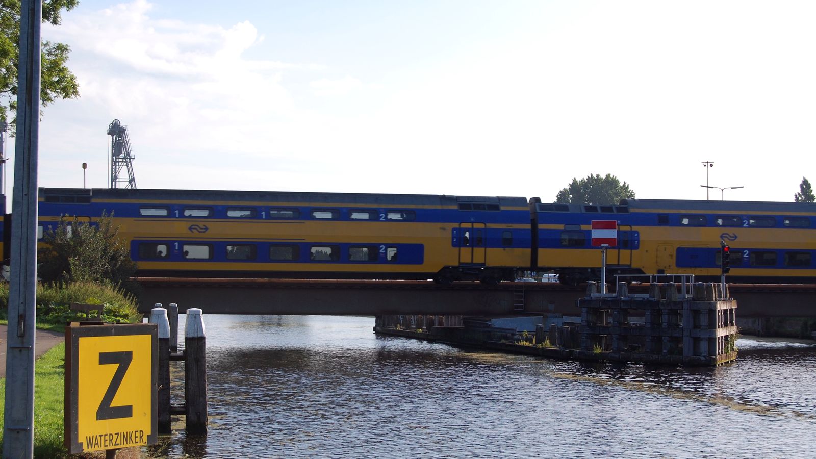 Een dubbeldekstrein van NS rijdt over de spoorbrug over de Gouwe in Alphen aan den Rijn, met de draaipijler in het water